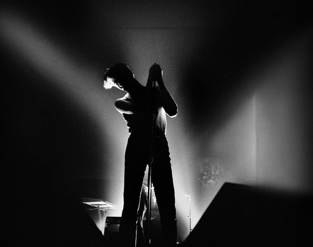 Black and white photo of Susan Ann Sulley of The Human League performing at Spit on Lansdowne Street in Boston. She stands at the mic with bright lights behind her but she’s only seen in silhouette.