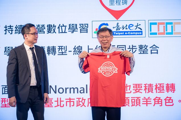 Photo of Vincent Hsieh (LAW’92) (left) and Ko Wen-Je, the mayor of Taipei (right), who holds up a red t-shirt that says “Boston U” on it. Behind him, a large screen with Chinese characters is seen.
