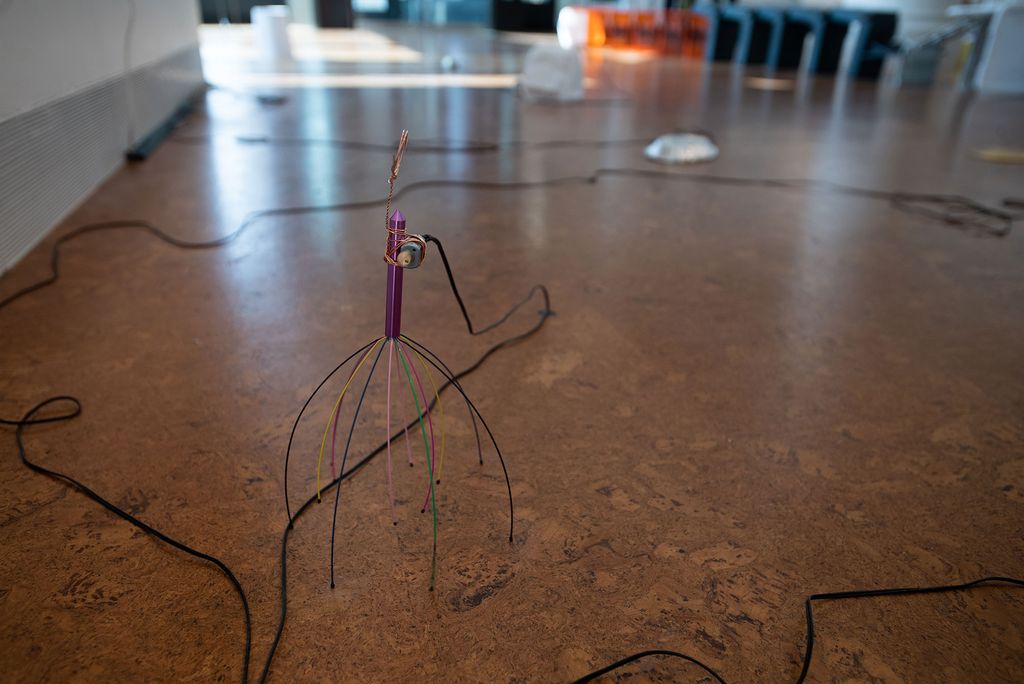 Photo of an element of Chang Wu’s (MFA’20) sculpture, “The Stuff -As -Dreams Are Made -On. The sculpture looks like a scalp massager, and rests on the ground of the gallery surrounded by black wires.