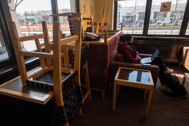 Photo of Maria Torres (CGS’21, COM’23) studying for her humanities class March 17 in the lobby of CGS. She wears a maroon sweatshirt and sits alone in the lobby, where most of the chairs are stacked on top of tables to ensure social distancing.