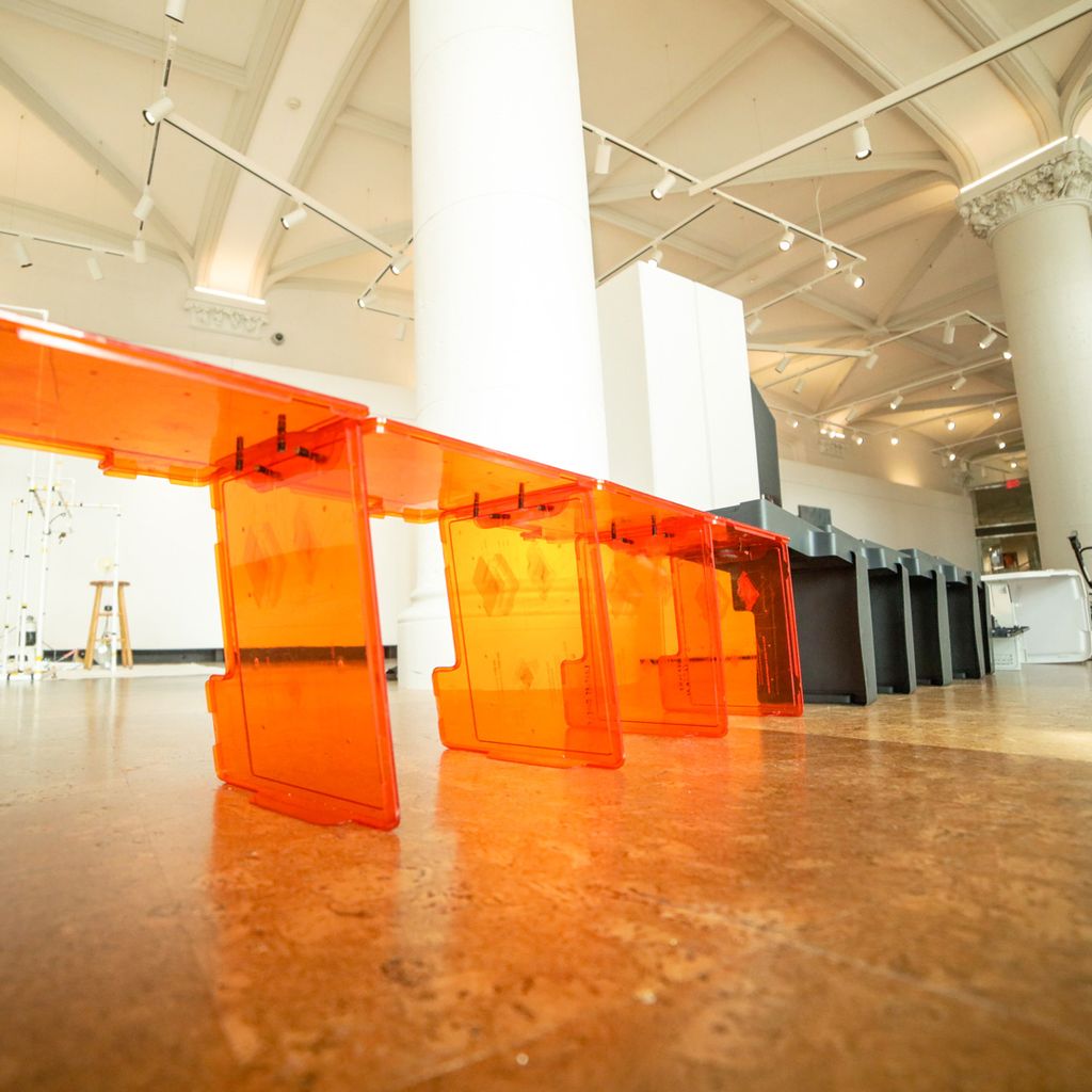 Photo of Ania Garcia Llorente's sculpture, which is a series of orange and black pieces of plastic lined up in a row to make a small wall through the gallery.