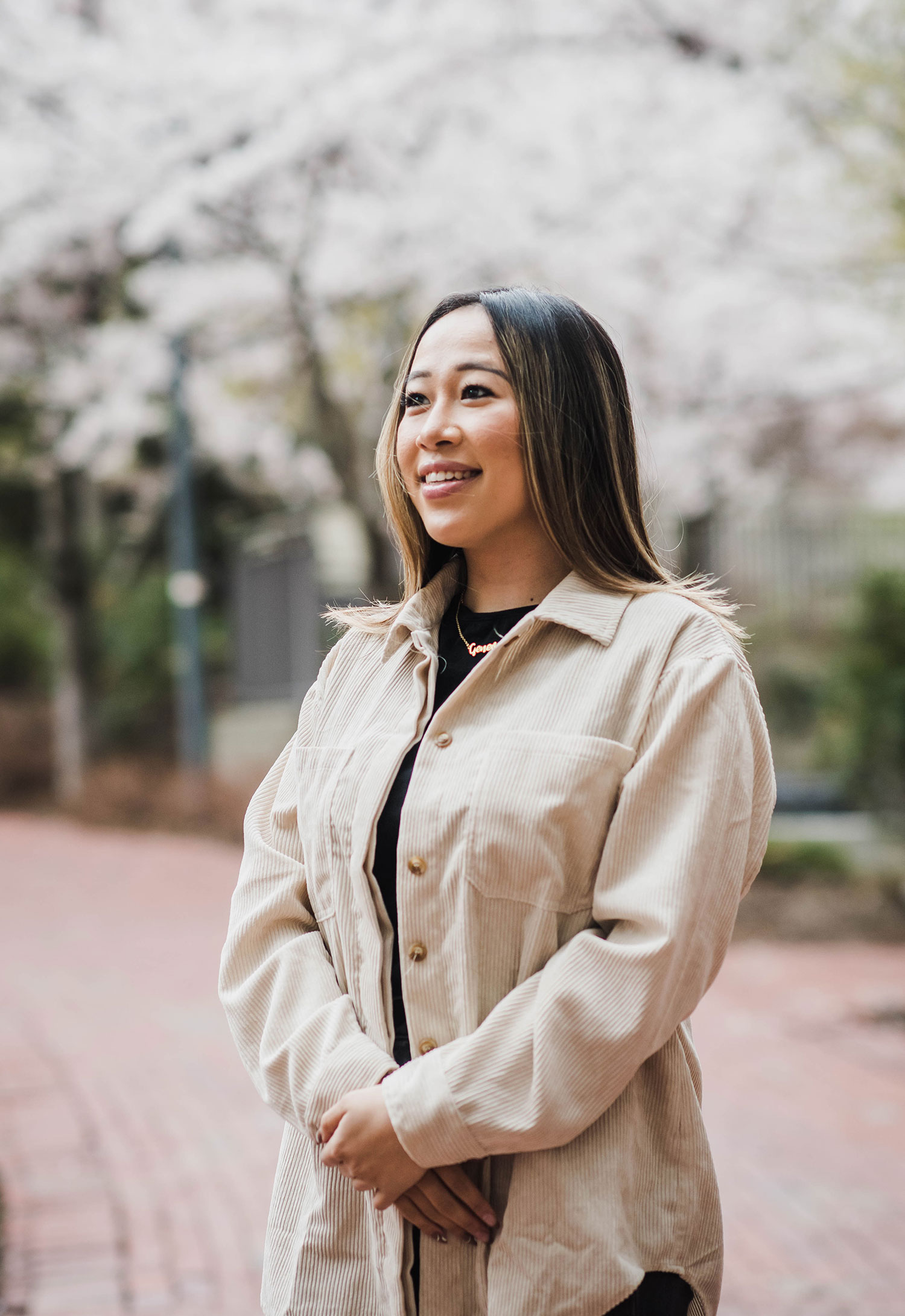 Photo of Geneve Lau (COM’21) in a tan spring coat, looking into the middle distance. She has long brown hair with streaks of blonde.