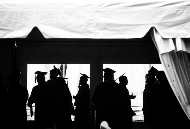 Graduating seniors in caps and gowns at BU Commencement in a tent silhouetted against white light