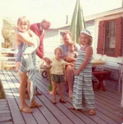 Blurry film photos the author (left) with her grandfather, father, and siblings on the back porch of the bungalow, in the late 1970s. Two young girls at the front wrap towels around themselves, other kids sit on the lap of an adult sitting at a picnic table.