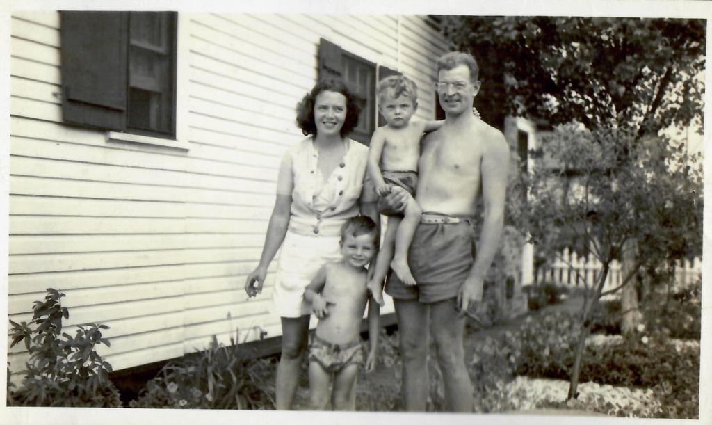 Black and white photo of the author’s grandmother, grandfather, father, and uncle by the Breezy Point bungalow in 1944. The kids and grandfather wear swim trucks and the grandmother wears a white summery outfit.