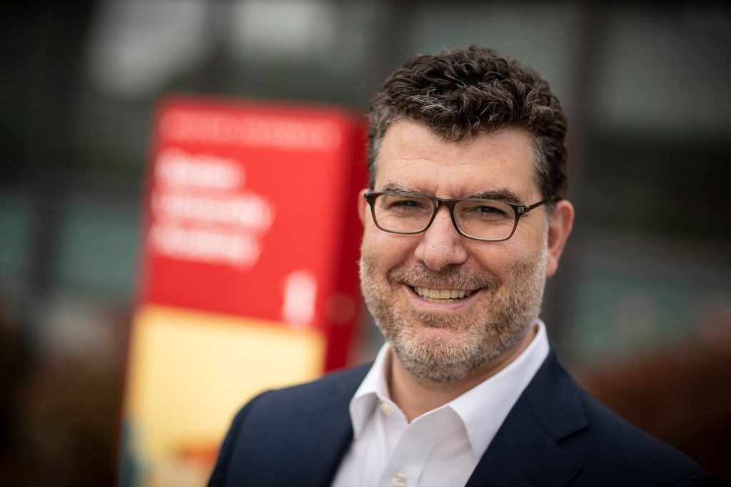 Headshot of Christos Kolovos, BU Academy head of school, in a blue suit and white collared shirt. He wears glasses and has a salt and pepper beard.