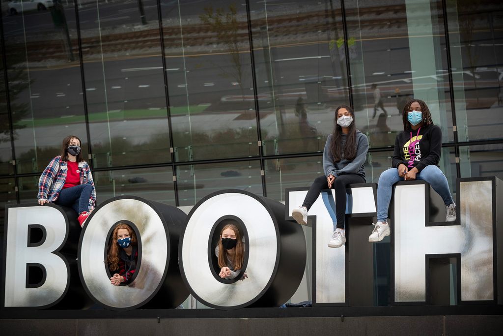 Photo of BU Academy students sitting on top of and in the letter ’O’s of the larger BOOTH sign outside of the Booth Theater. Students include: Ioanna Weiden (BUA’24) (from left), Jasper Milstein (BUA’24), Sally Jamrog (BUA’23), Safiya Karim (BUA’24), and Jovanah Noelsaint (BUA’24). Each student wears a face mask and most wear jeans and a sweatshirt.