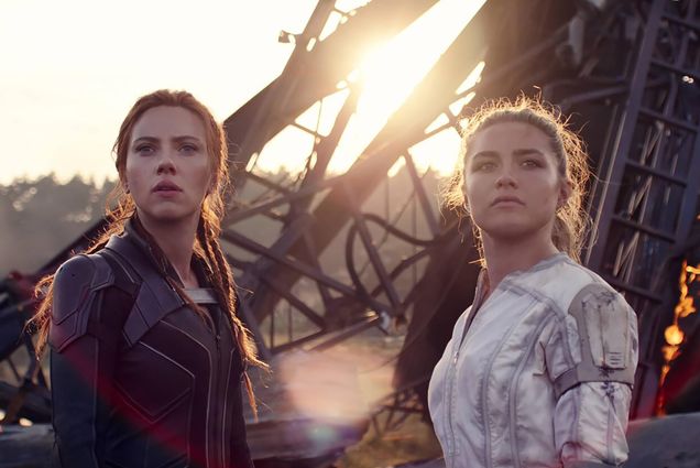 Movie still from Black Widow, starring Scarlett Johannson as Natasha Romanoff/Black Widow, at left, wearing a black leather jacket, next to Florence Pugh playing her little sister, Yelena Belova. Behind them, some rubble is seen in the distance.