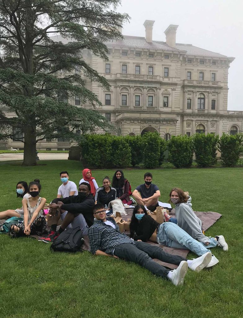 Photo of students sitting on a blanket and lunching on the lawn of a Rhode Island mansion during a field trip. It is a foggy day.