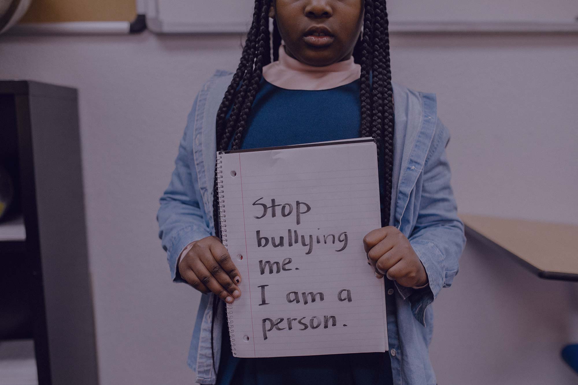 An African American school girl holds a handwritten sign that says 'Stop bullying me. I am a person.'