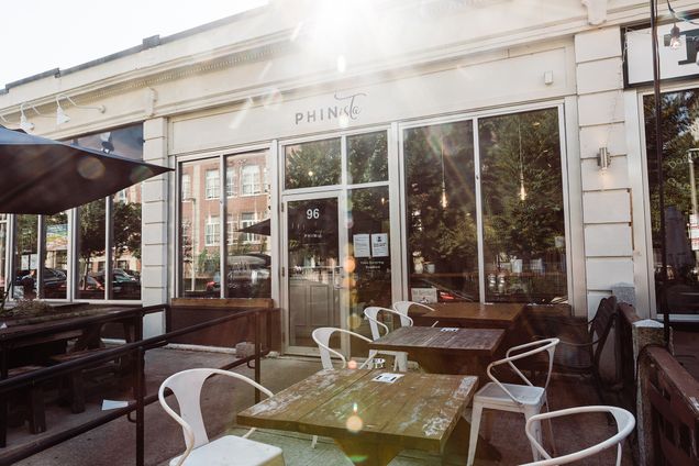 exterior photo of outdoor coffee shop seating with a sun glare highlighting the shop's sign and entrance.