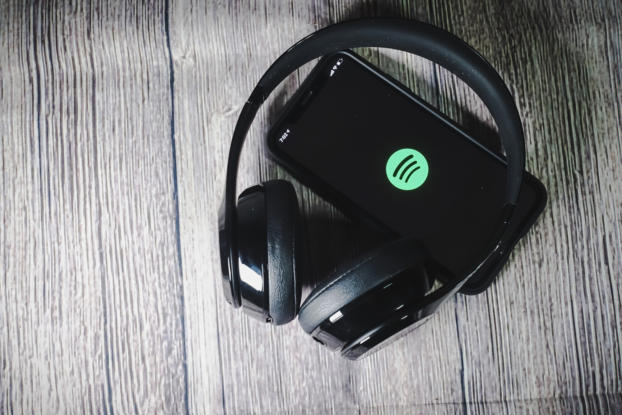 An iphone 11 screen showing spotify icon with Beats headphones lying on a wooden tabletop