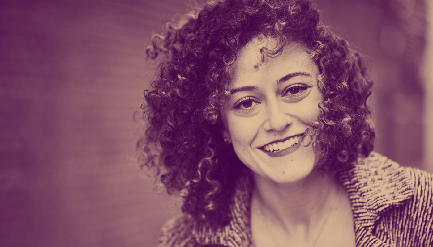 Portrait of Danielle Letayf, founder of the start-up business Badassery, outside with a brick wall in the background. Photo is color treated with a dark yellowish purple tint.
