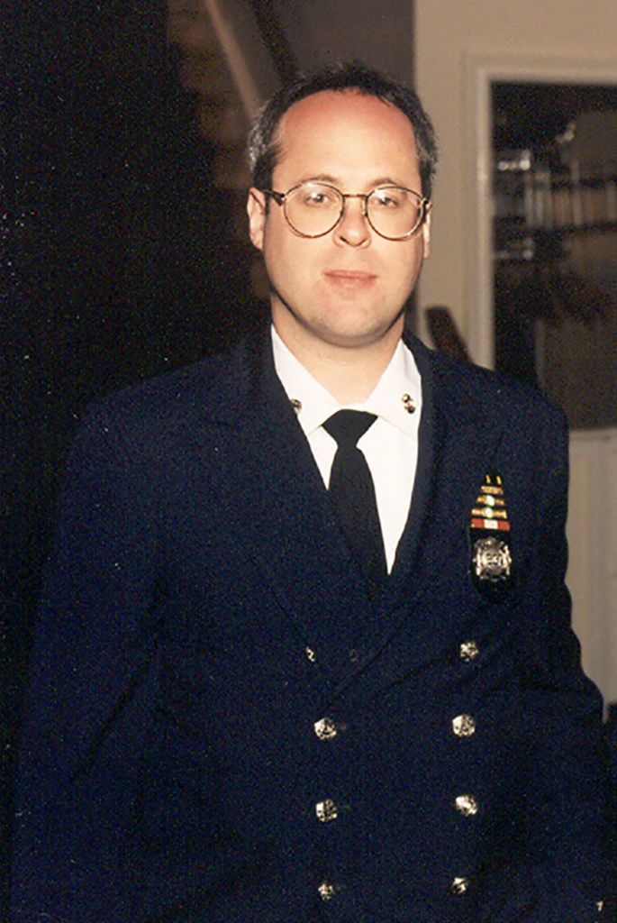 photo of a printed photo of Glenn Winuk in a blue dress uniform. He wears large circular glasses.