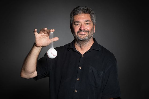 Professor Andy Andres dangles a baseball stuck to his finger with Spider Tack adhesive, a commonly used sticky substance in Major League Baseball