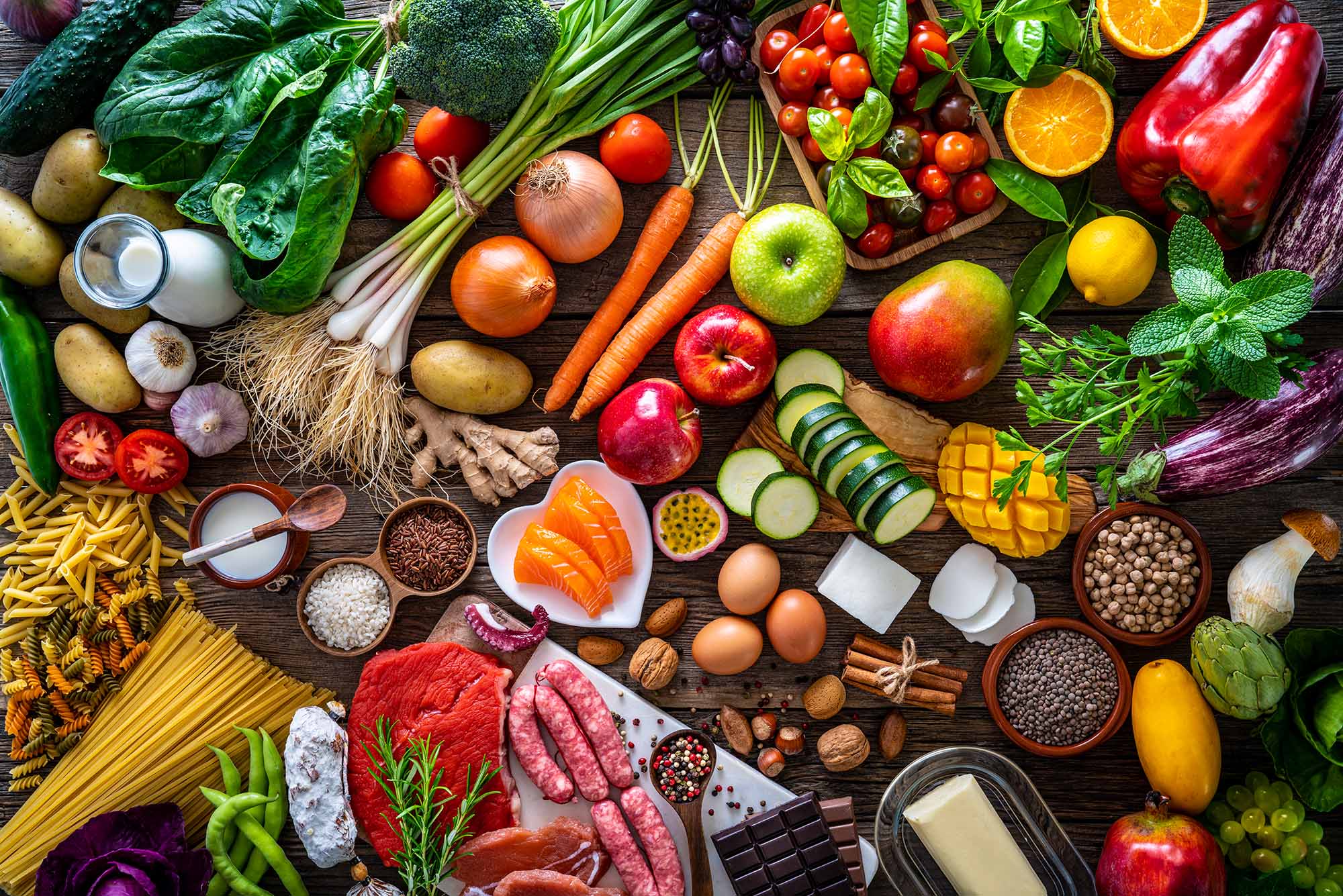 Aerial photo of a rustic table filled with fruits, vegetables, pasta, milk, nuts, and more.