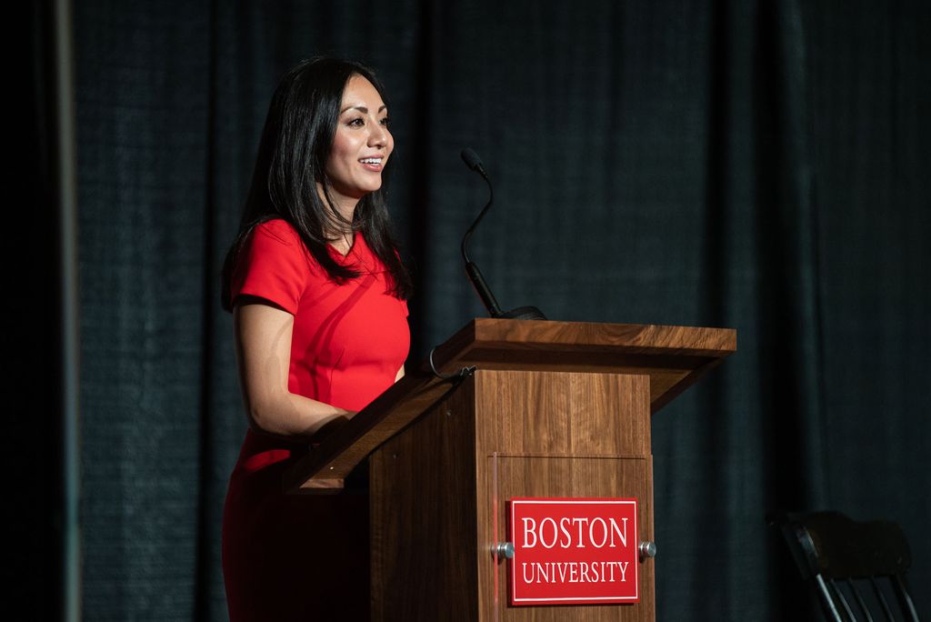 Photo of Monica Wang, an SPH associate professor of community health sciences, in a red dress, speaking at the podium and smiling.