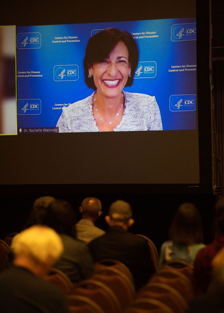 Photo of Dr. Rochelle Walensky, Director of the Centers for Disease Control and Prevention on a projected screen at What the Science Tells Us: Racial Health and Economic Inequities during the Pandemic Symposium presented by The BU Center for Antiracist Research in the Metcalf Hall October 1. She smiles wide and sits in front of a blue CDC background.