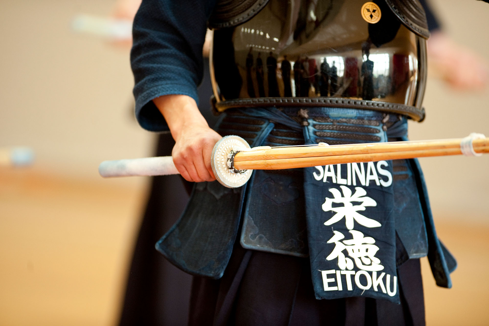 photo of a person in a kendo stance, holding a long wooden stick, and wearing a navy uniform and black reflective chest protector.