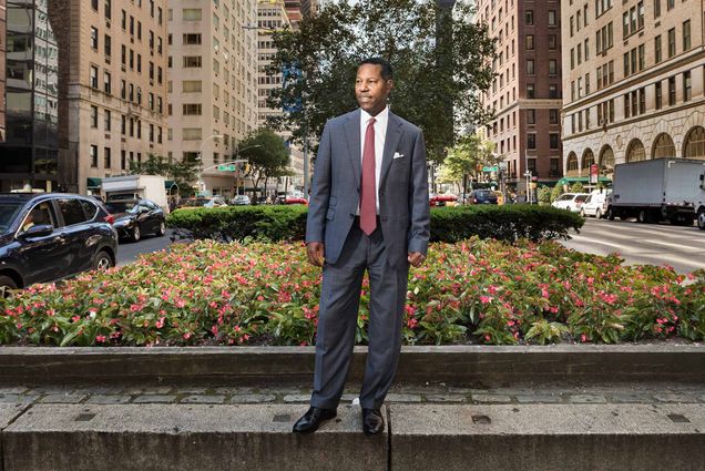 Portrait of Questrom alum David R. Jones in New York City. He stands and looks to the left in front of a large patch of pink flowers. He is surrounded by NYC traffic and looming building as backdrop.