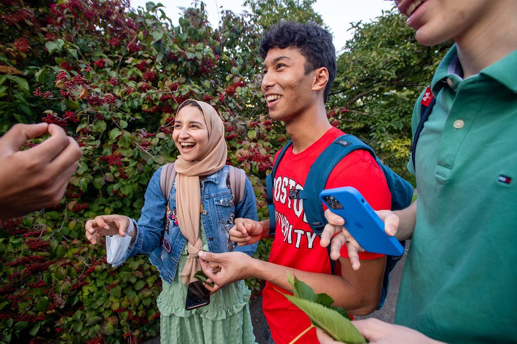 photo of Nourhan El Sherif (ENG’24) from left, Nashr El Auliya (ENG’24), and Tyler Critz (CAS’24) as they take a closer look at and have a taste of Viburnum berries during a tour of the Arnold Arboretum. The background is full of touring berry bushes and the students share looks of excitement as they hold purple berries in hand.