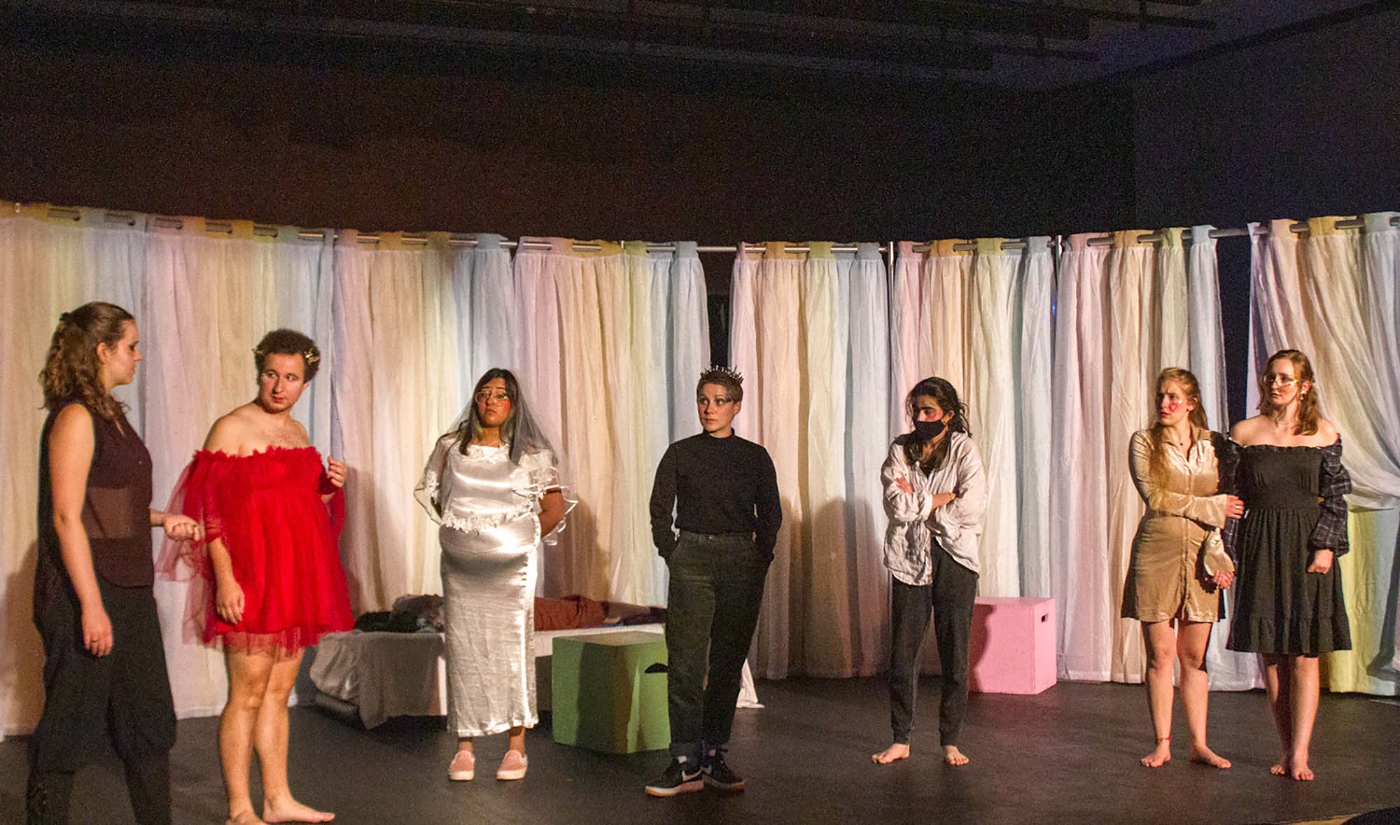 Photo of a rehearsal featuring: fEmma Permé (CAS'22) as Demetrius, Ian Aquino (COM'23) as Helena, Anoushka Thakur (CAS’23) as Hippolyta (she also plays Titania), Elizabeth Kostina (CAS'24) as Theseus, Gayane Kaligian (CAS'22) as Egeus, Carolyn (Carrie) Welter (CAS'22) as Hermia, and Ella Moran (CAS'25) as Lysander. They all wear shiny clothing, and rainbow pastel-colored curtains hang behind them.