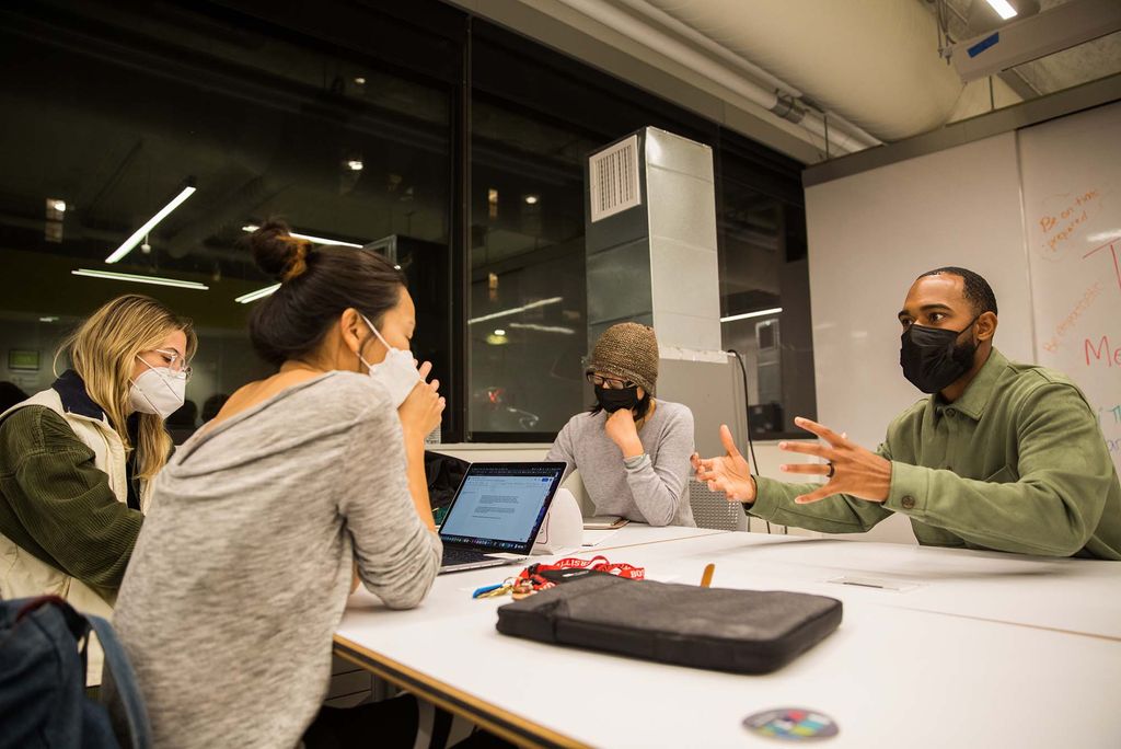 Photo of Jonathan Allen, right, chatting with, clockwise from left, Kati Nalbandien (MET’22), Sohyoung Park (CFA’23) and Elle Zeng (MET’22) about their self sustaining ecosystem project during a a speed mentoring session at the BUild Lab Monday, October 25, 2021. The group wears face masks and sits around a white table with their laptop open.