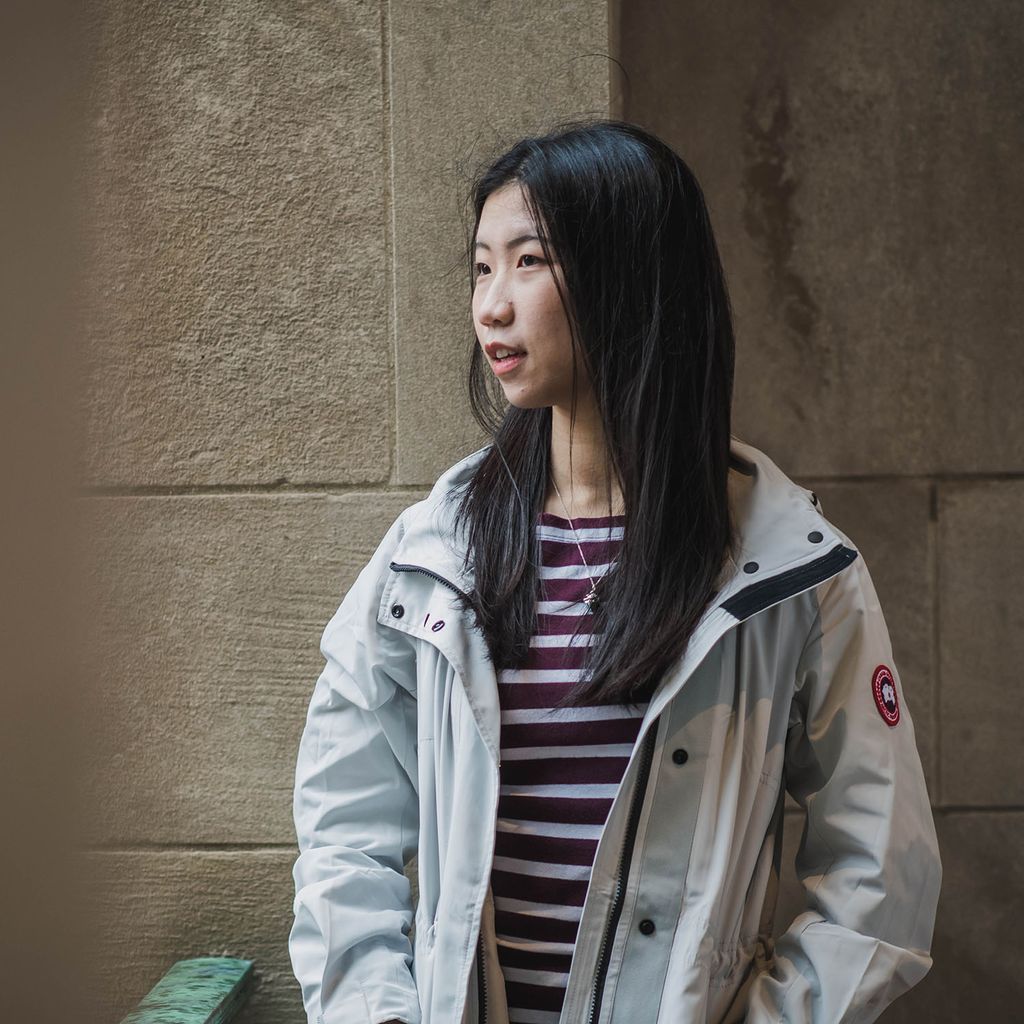 photo of Shilu Wang on BU's campus. She wears a burgundy and grey striped shirt and a light blue Canada Goose jacket as she faces the left and looks off into the distance.