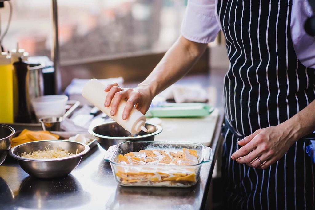 Photo of chef Kate Smith drizzling sauce over the butternut squash and potato gratin as she assembles it. 