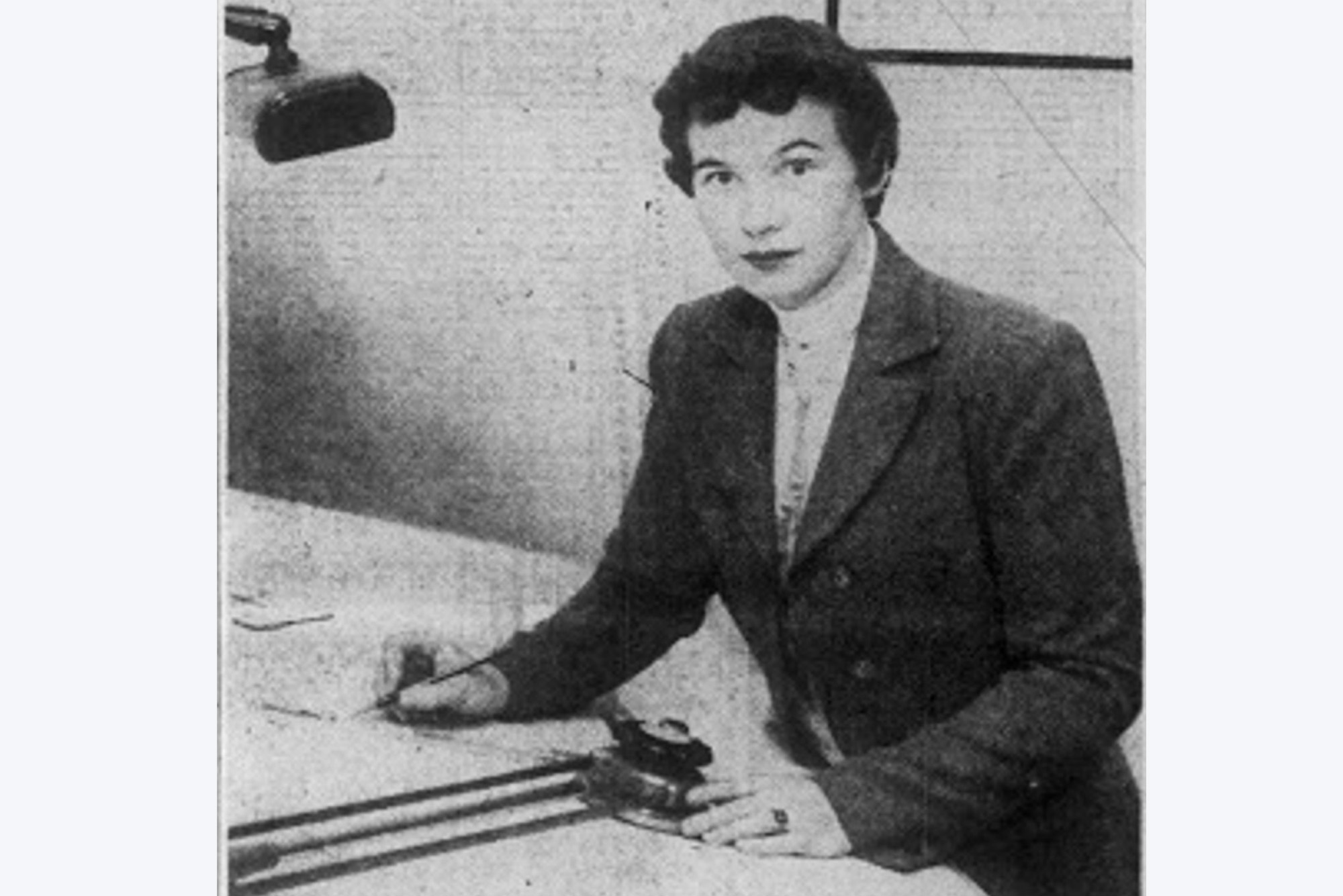 Photo of Anne Everest Wojtkowski (1935-2014), the first woman to graduate from the Boston University College of Industrial Technology. The photo is black and white and pictures Wojtkowski writing at a desk with a lamp. She has short dark hair.