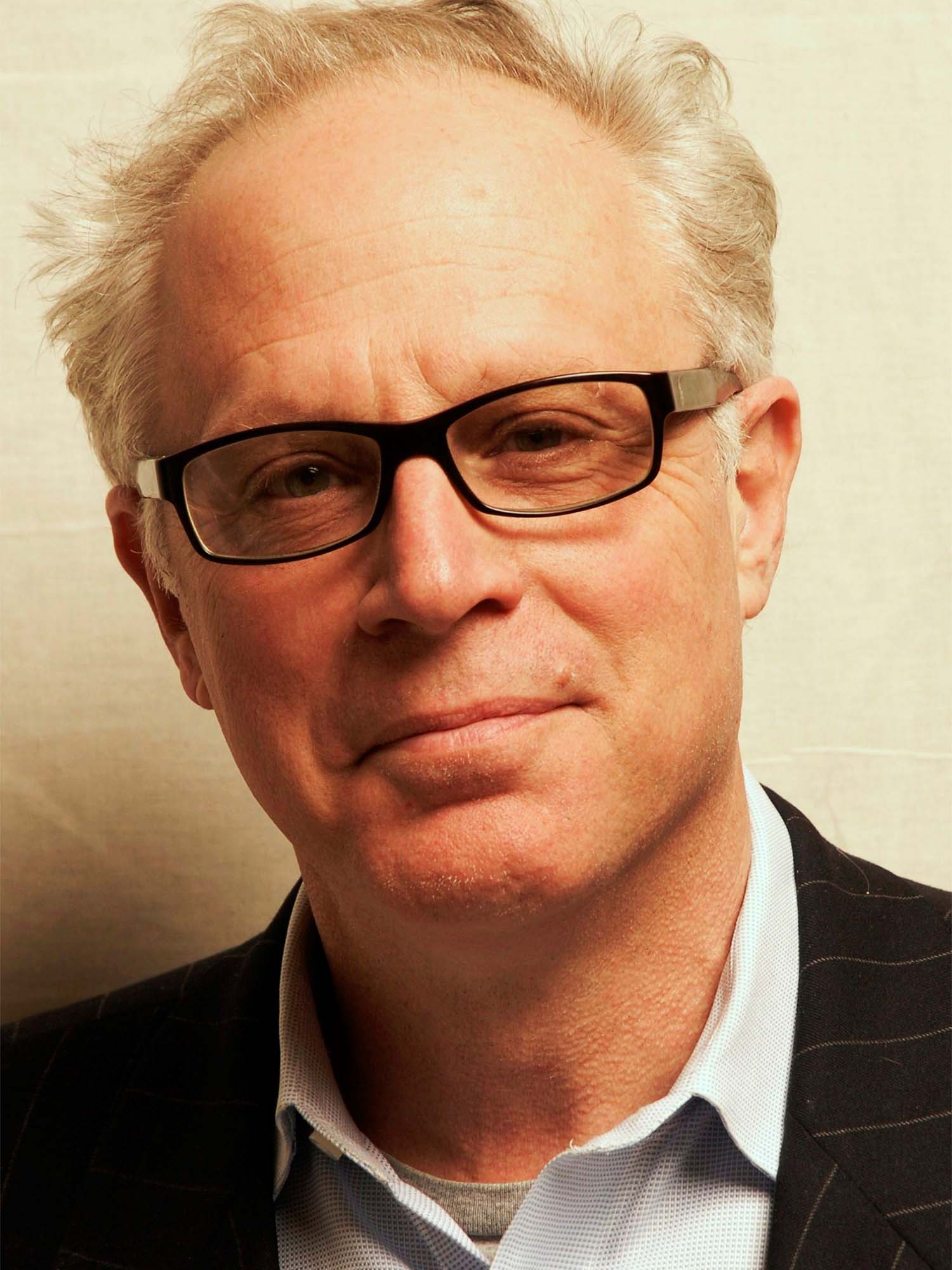 Ivan Schwartz in a suit jacket and dress shirt wearing glasses in front of a beige background