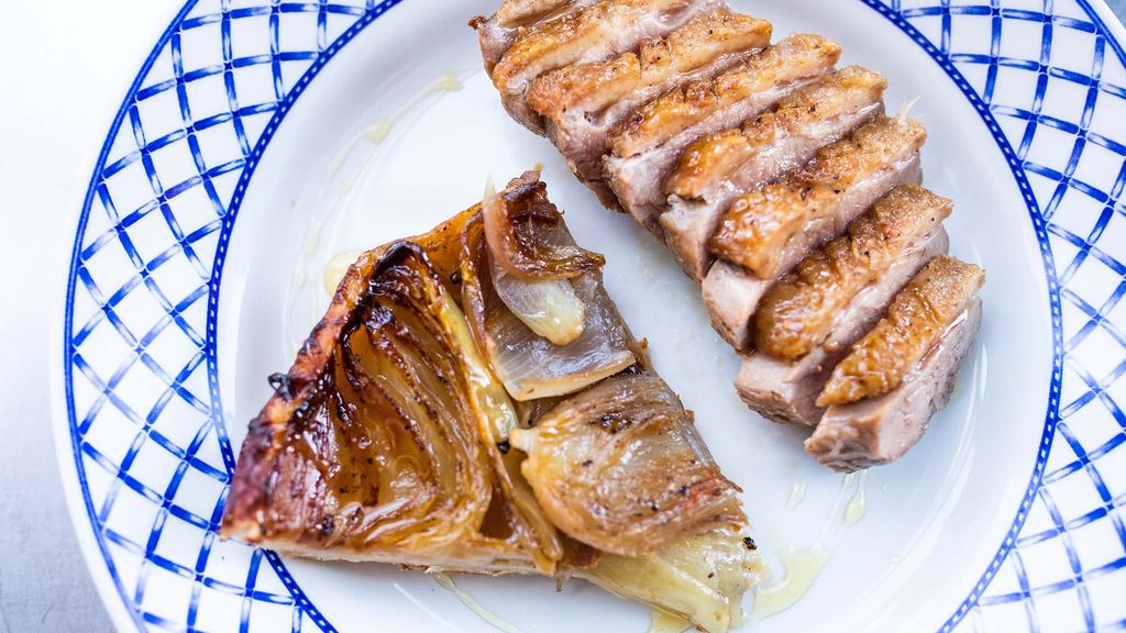 Photo of a sliced Duck Breast and Onion Tarte Tatin on a white plate with a blue border.