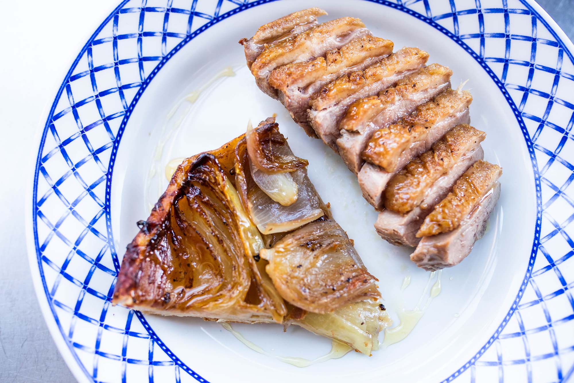 Photo of a sliced Duck Breast and Onion Tarte Tatin on a white plate with a blue border.