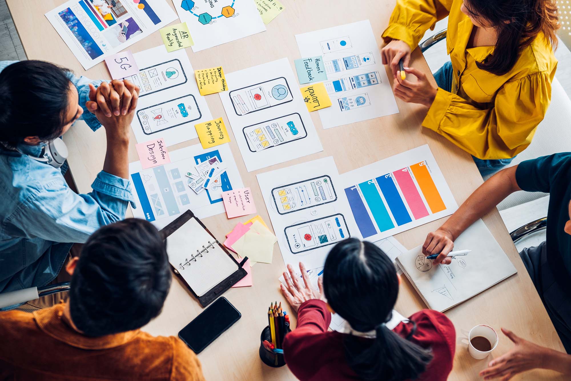 Top view photo of Asian ux developers and ui designers brainstorming about mobile app interface on a table with customer brief and color code in a modern office