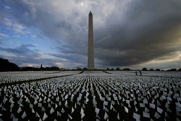 Photo of a field of white flags around the Washington Monument. Artist Suzanne Brennan Firstenberg’s temporary art installation on the National Mall, In America: Remember, features white flags that symbolize a life lost to COVID-19. Behind the mall, the sky is ominous and dark.