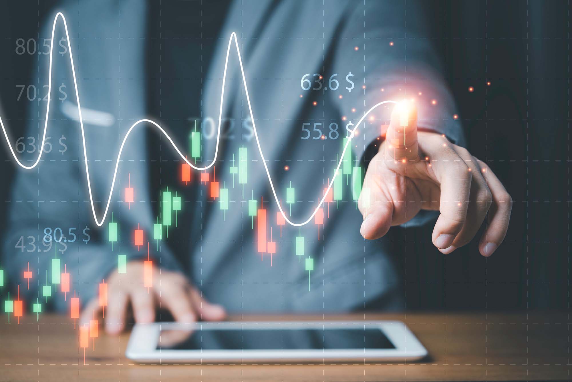 Photo of a person using an ipad with one hand and drawing a graph with their finger of the other hand. The line graph is white and surrounded by numbers and red and green bars.
