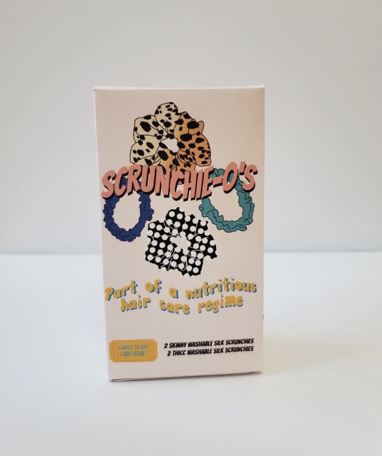 photo of a package of Scrunchie-os, a pink box featuring illustrations of scrunchies. Box reads "Scrunchie-os, part of a nutritious hair care regime"