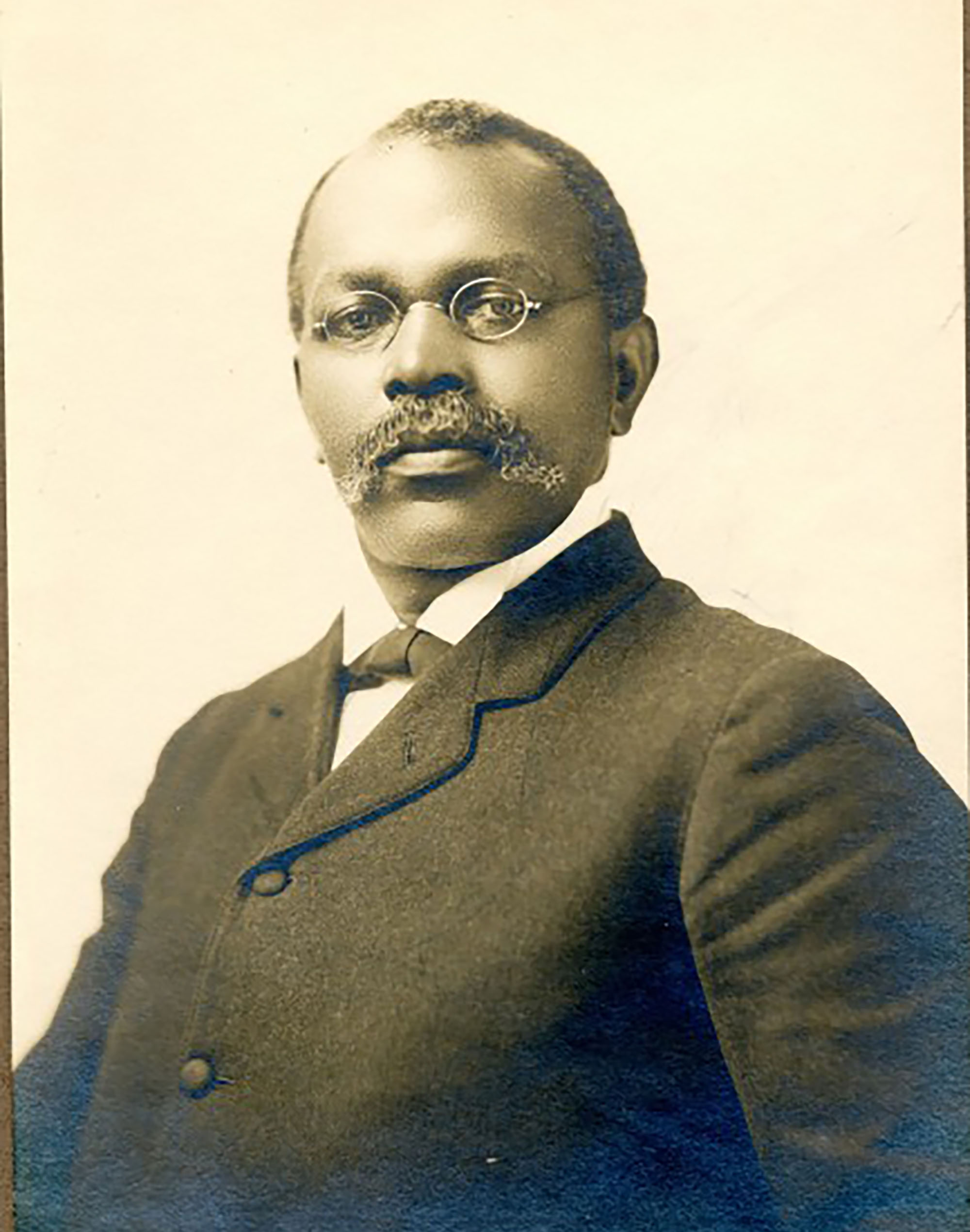 Photo: An old portrait of J.W. Bowen, a Black man wearing a tailored suit and small, wire spectacles.