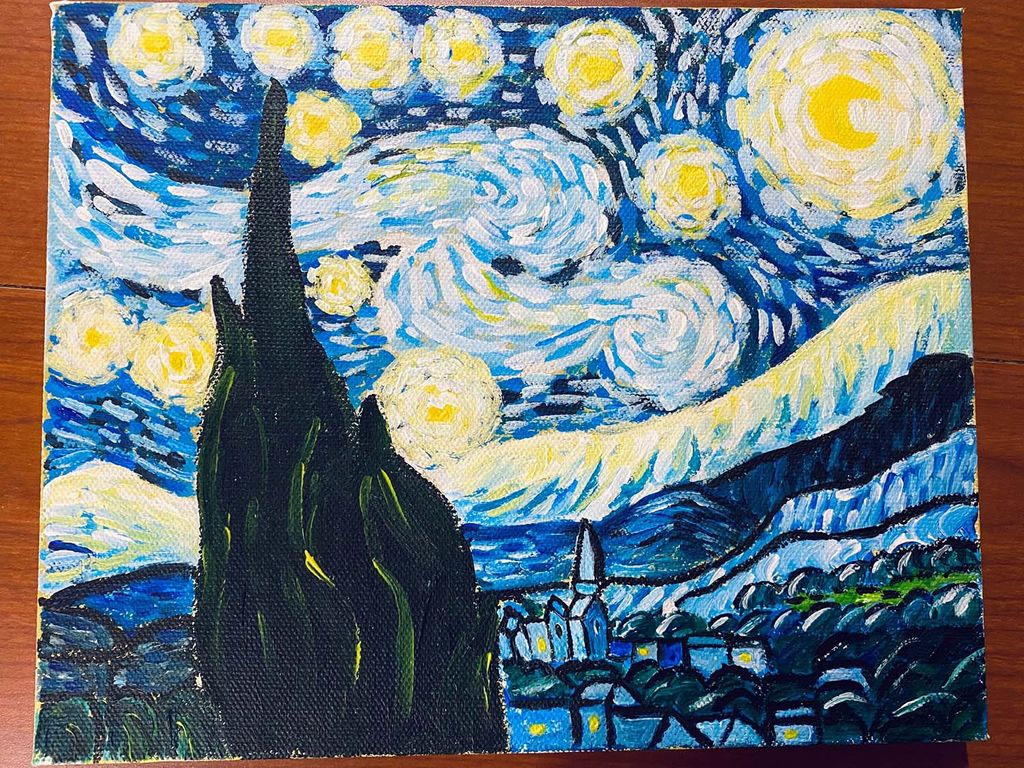 photo of yin's rendition of Van Gogh's starry night on a canvas, which rests on a wooden floor in the photo. The painting has a large dark green hedge in the foreground, a town in the background and large swirling clouds in the sky.