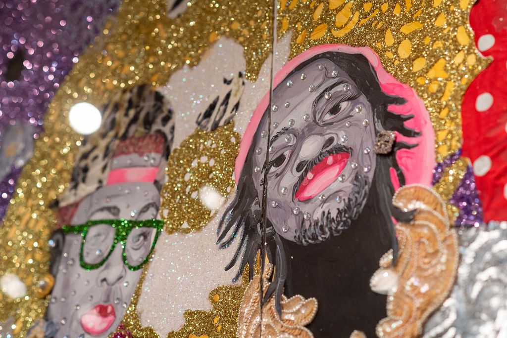 Closeup of Ebony G. Patterson’s II Trees in a Forest. The closeup features the painted portraits of two Black people, one with green glasses and a cheetah print hat, and one with short locs and bright pink lips. Both portraits are on a swirling golden background and the whole piece is bejeweled.