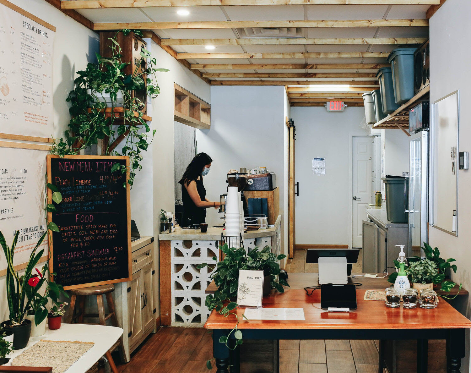 Photo: Interior of Glasser Coffee Co. A small bright coffee shop, with wood and greenery tones. A worker stands at the cash register as coffee paraphernalia is on display.