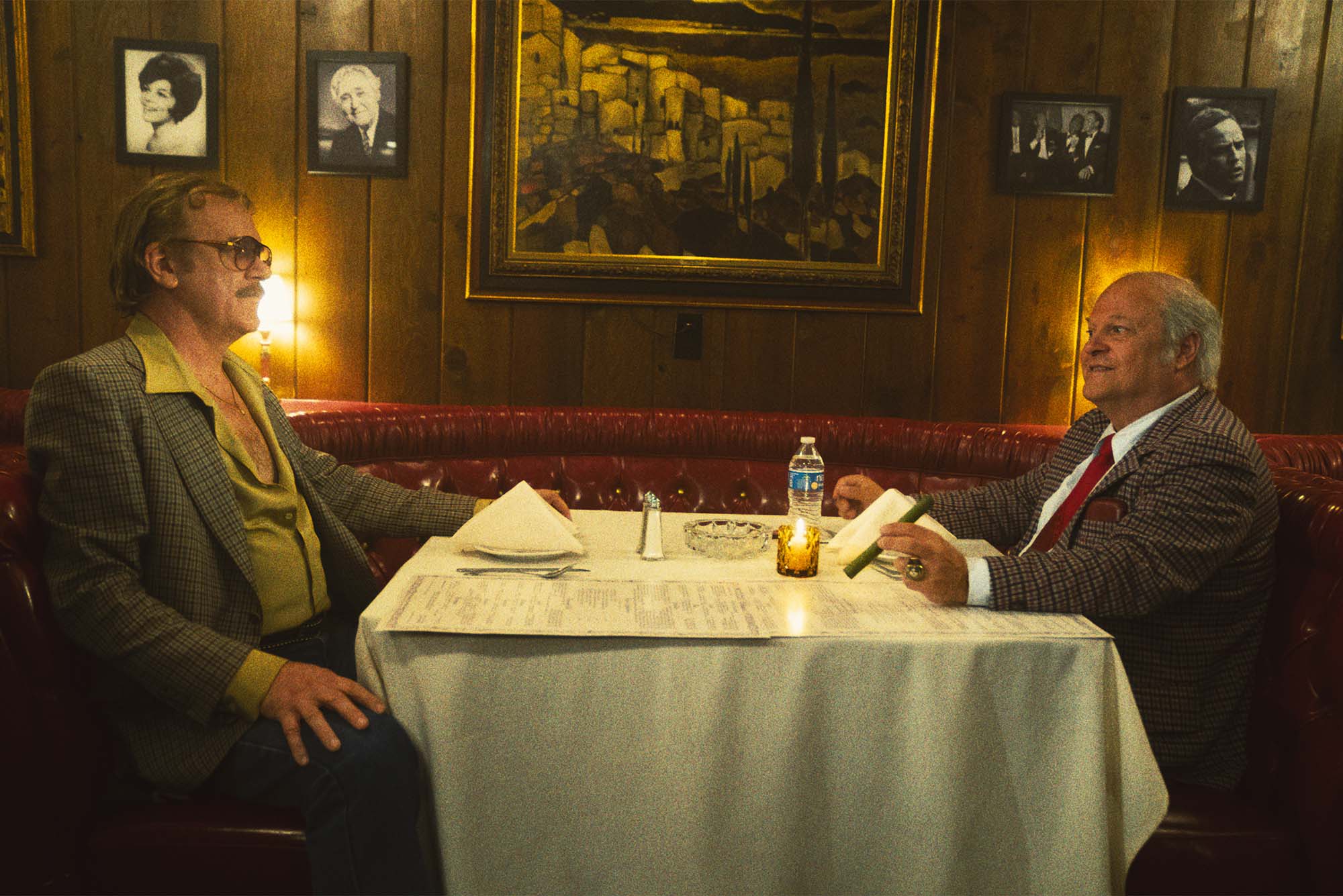 Two men in suits sit opposite each other in a fancy restaurant