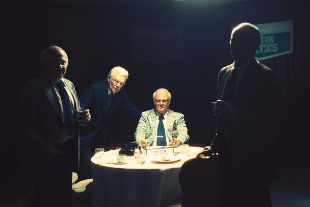 A group of men stand in a dark room with a bright white light on Michael Chiklis portraying Red Auerbach