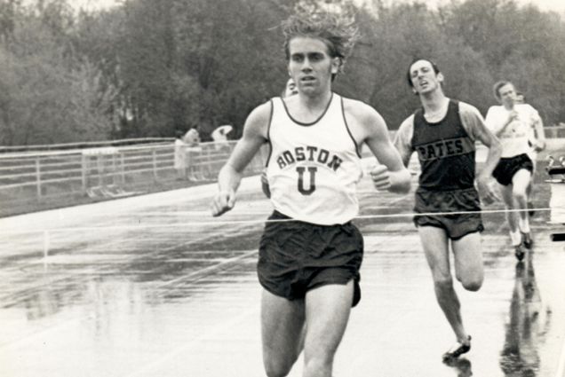 Black and white photo of Tom Beatty (CAS’72) during a historic track meet. He wears a BU jersey and his hair bounces as he runs ahead of two competitors on a track.
