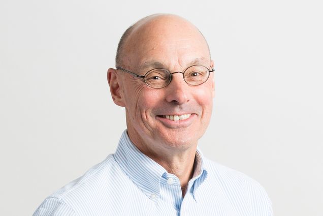 Headshot of Christopher Cakebread, who wears round glasses and a white and blue pinstripe button-up shirt.