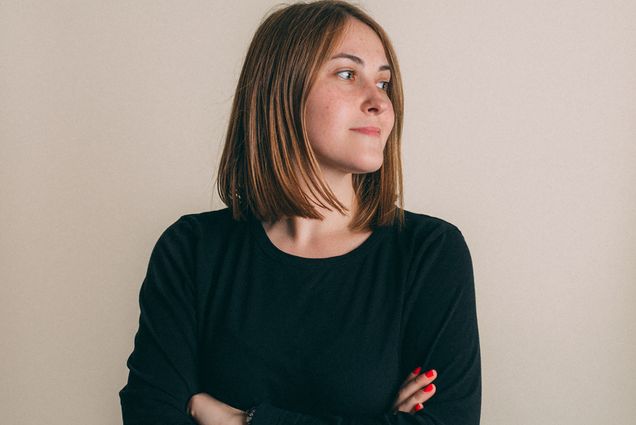 Headshot of Emma Johnson. A young white woman with short brown hair and wearing a long-sleeved black shirt smiles and looks off to the right with arms crossed.