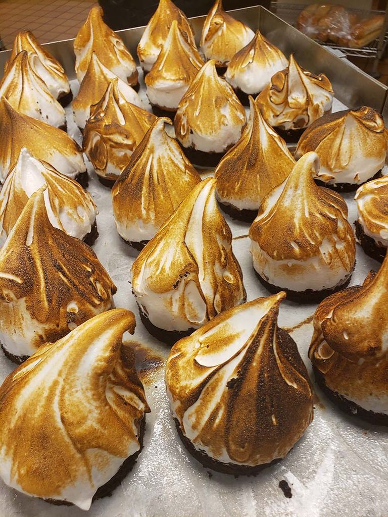 Photo of S'mores mousse bombs with smoked 65 percent chocolate mousse, cayenne toasted marshmallow, and chocolate buttermilk cake. Little peaks of torched whipped mousse sit evenly lined on a tray