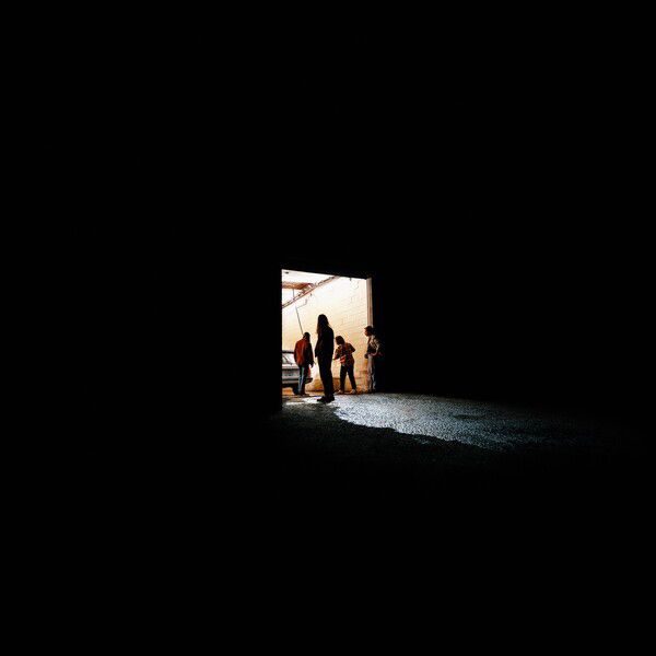 Album cover of Peach Pit's "From 2 to 3". Image shows a zoomed out photo of a dark room and light coming in from an open door that a few people are walking into.