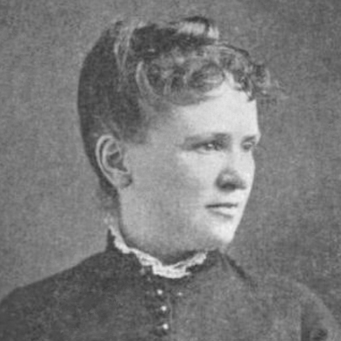 Black and white photo of Lelia Josephine Robinson. A white woman with hair in a neat, high bun looks to the right with a neutral expression. She wears a high neck button up dress.