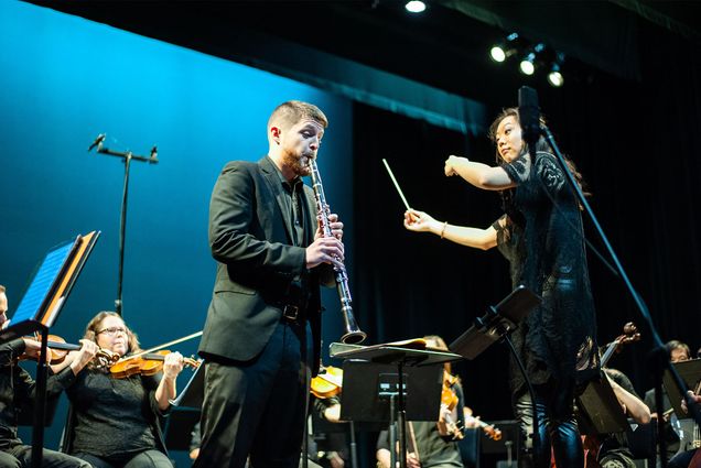 Nicholas Brown plays the clarinet as the conductor and orchestra accompany him